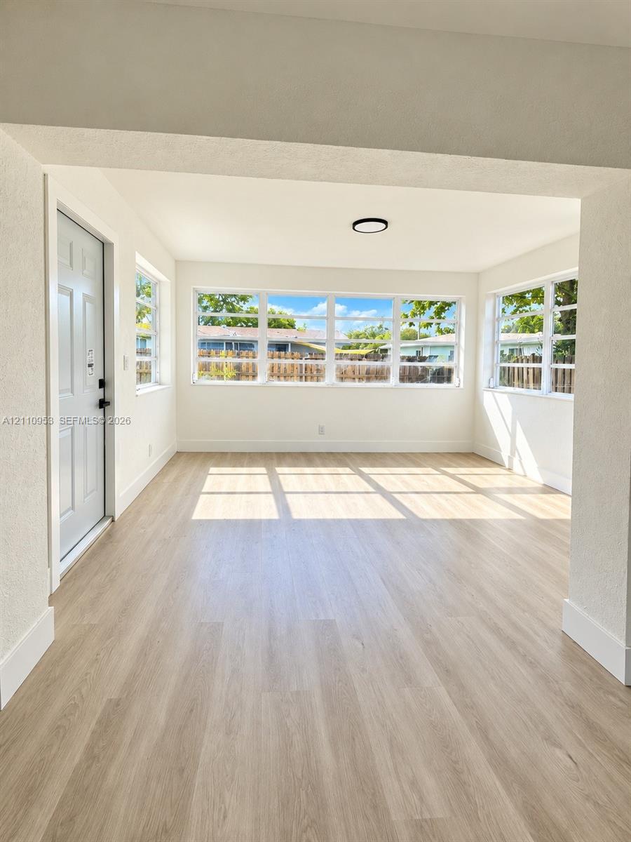Neutral color palette with wood-finish flooring, multiple windows providing natural illumination, and a flush-mount circular ceiling fixture