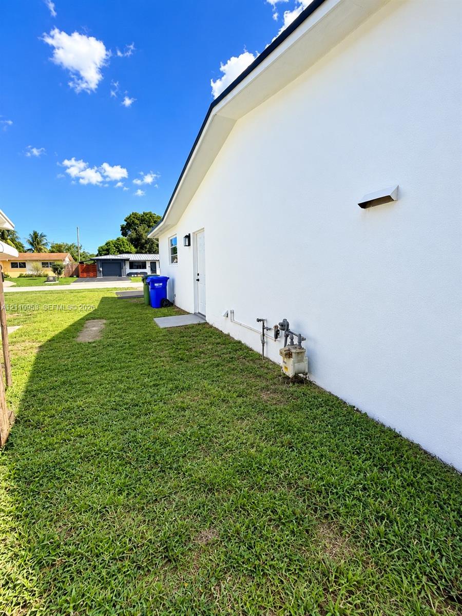 Exterior side profile featuring smooth white stucco siding, a solid entry door, and a grass-covered side yard
