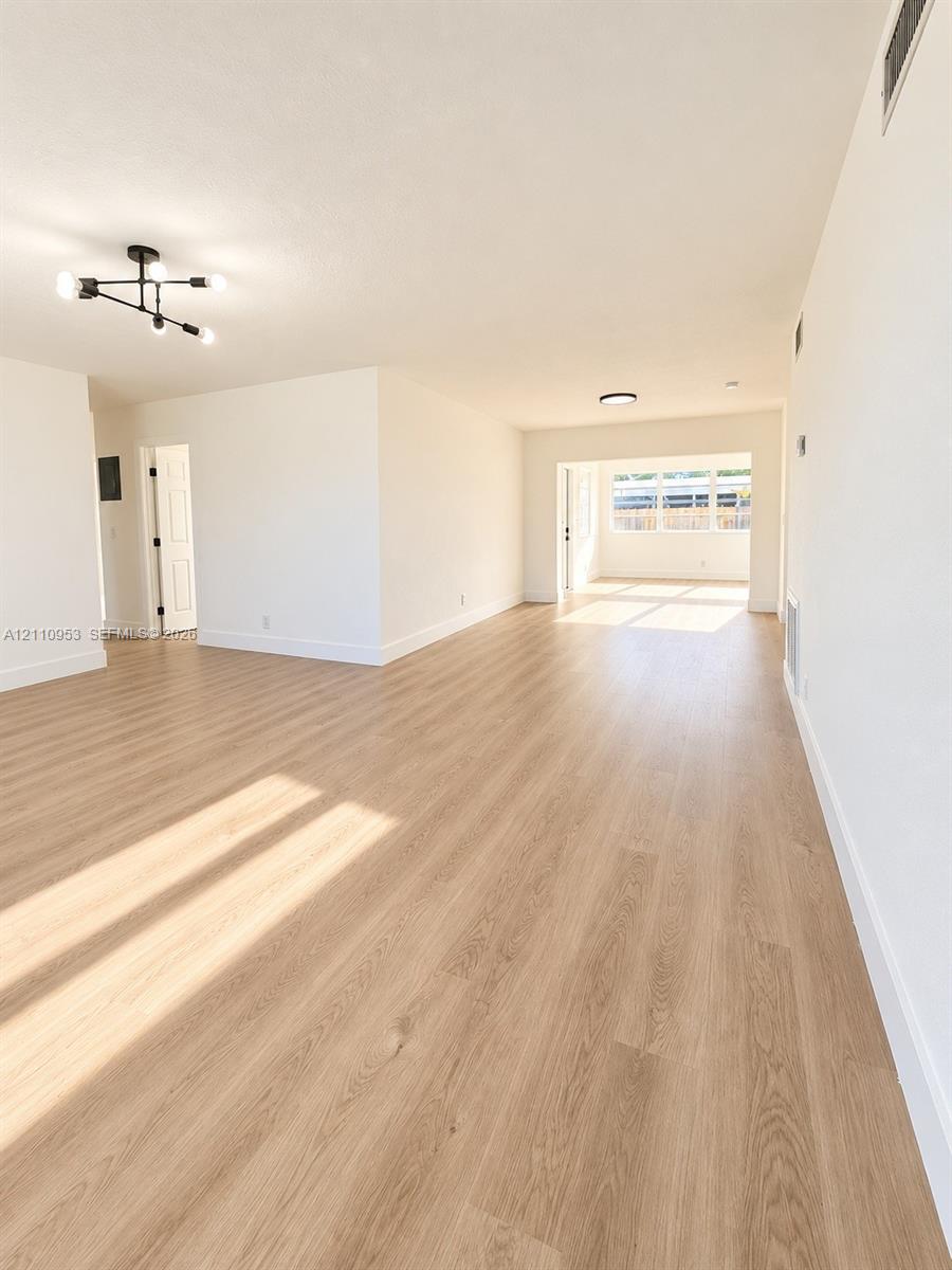 Open interior space featuring wood-finish flooring, neutral walls, and a multi-arm geometric ceiling fixture Open interior space featuring wood-finish flooring, neutral walls, and a multi-arm geometric ceiling fixture