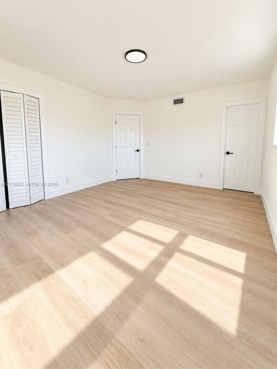 Interior room featuring wood-finish flooring, white walls, louvered closet doors, six-panel interior doors with matte black hardware, and a flush-mount circular ceiling light