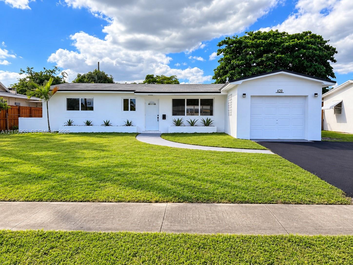 Single-story residence with white stucco exterior, integrated one-car garage, manicured front lawn, built-in concrete planters, and paved driveway