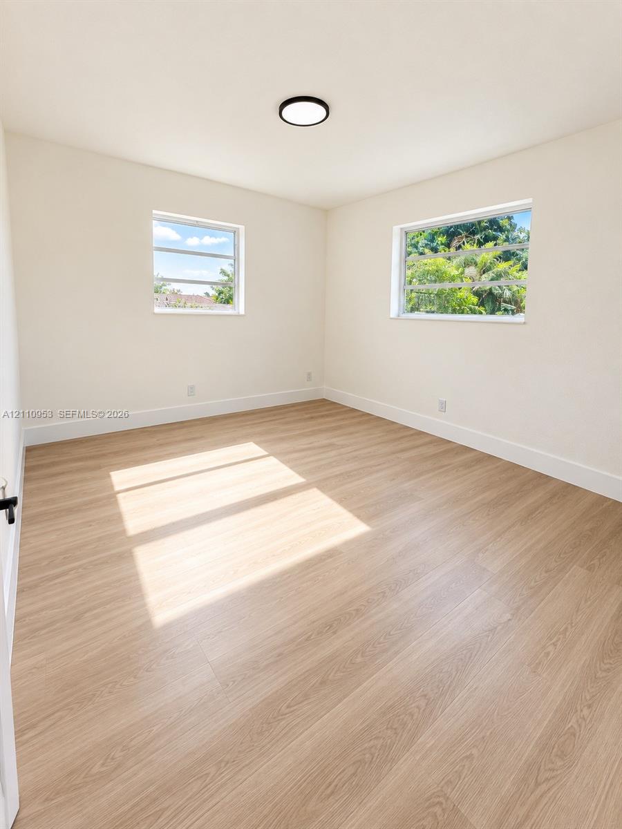 Neutral-toned room featuring wood-finish flooring, two jalousie windows, and a flush-mount circular ceiling fixture