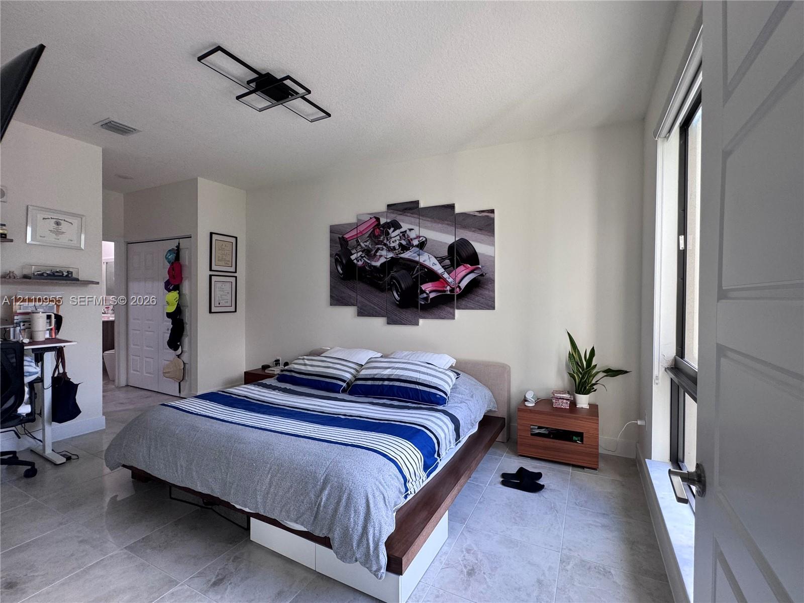 Neutral tile flooring, modern rectangular geometric ceiling light fixture, sliding panel closet doors, and large windows with exterior exposure