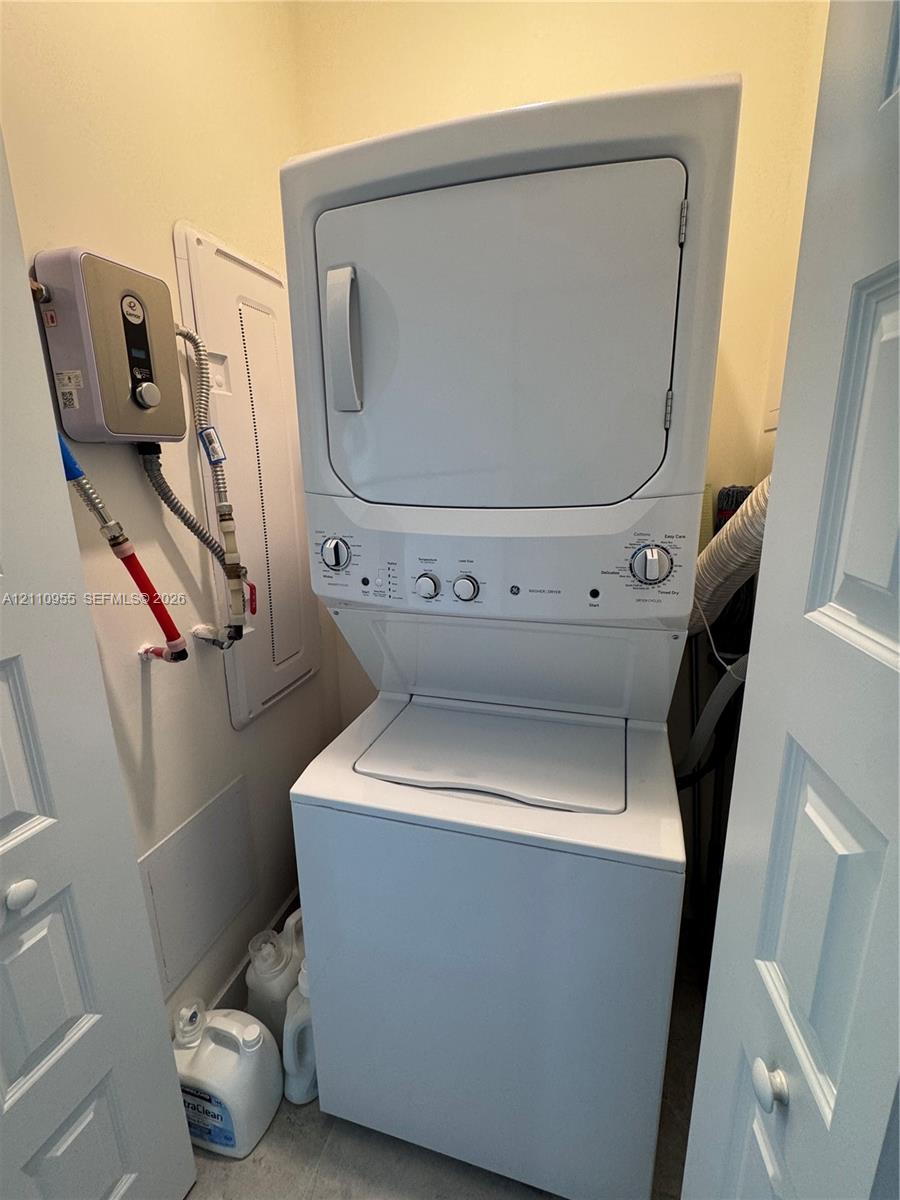 Stacked white laundry appliance center featuring a top-load washer, front-load dryer, and wall-mounted electric tankless water heater