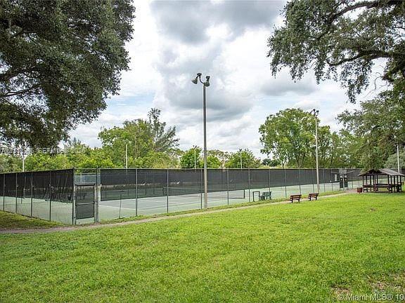 Tennis court facility enclosed by perimeter fencing, featuring integrated court lighting and a covered pavilion