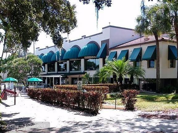 Two-story stucco exterior featuring arched windows, decorative green fabric awnings, a tile roof, and landscaped hedging