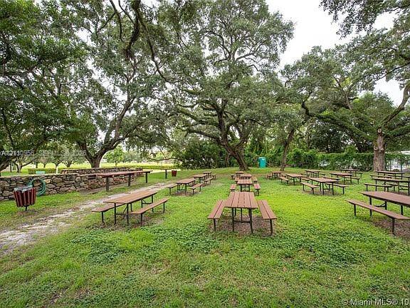 Expansive outdoor grounds featuring mature shade trees, a natural stone retaining wall, and multiple built-in wooden picnic tables