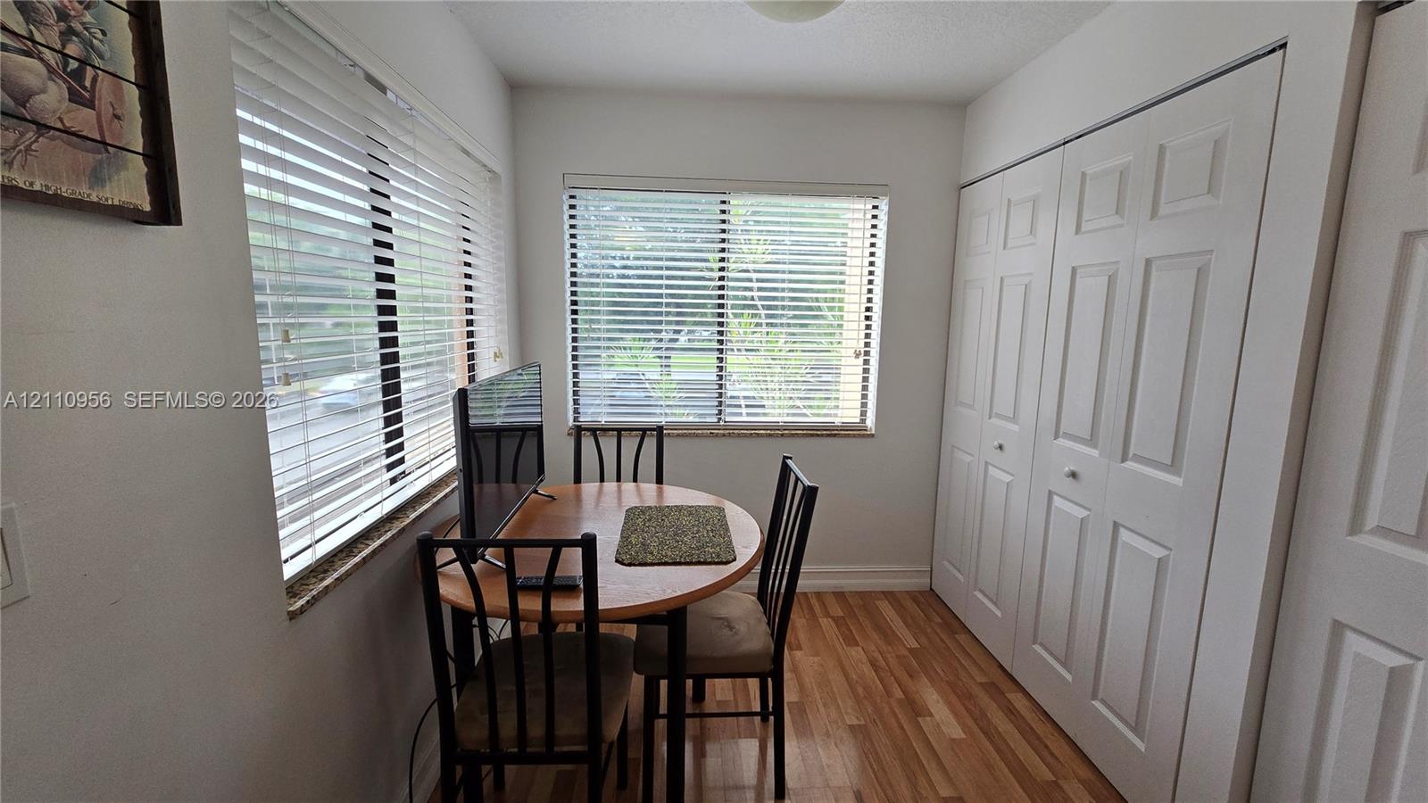 Neutral-toned interior room featuring wood-finish flooring, dual windows with horizontal blinds, and a large closet with paneled double-fold doors