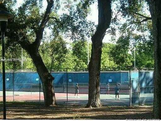 Tennis court enclosed with chain-link fencing, situated within a setting of mature trees