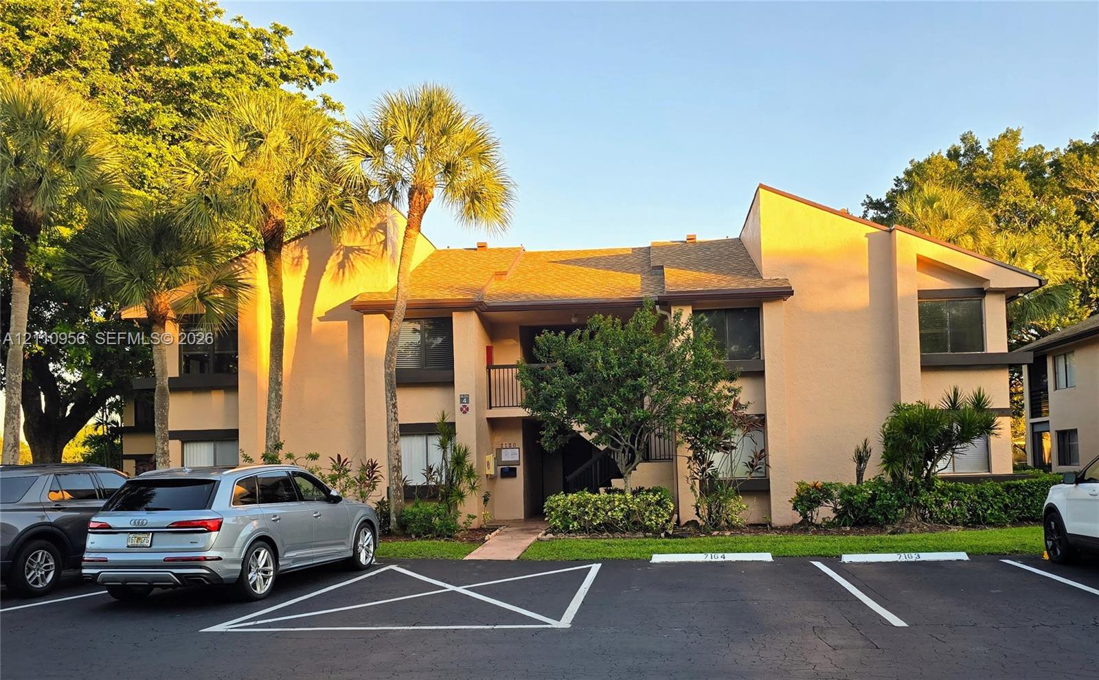 Two-story exterior featuring a textured stucco facade, asphalt shingle roof, integrated balconies, and mature palm tree landscaping