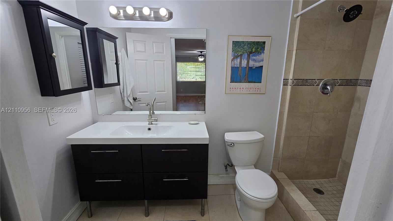 Bathroom featuring a modern floating vanity with a white countertop and rectangular basin, a wall-mounted mirrored medicine cabinet, a four-bulb light fixture, and a tile-surround shower with a metallic rain shower head
