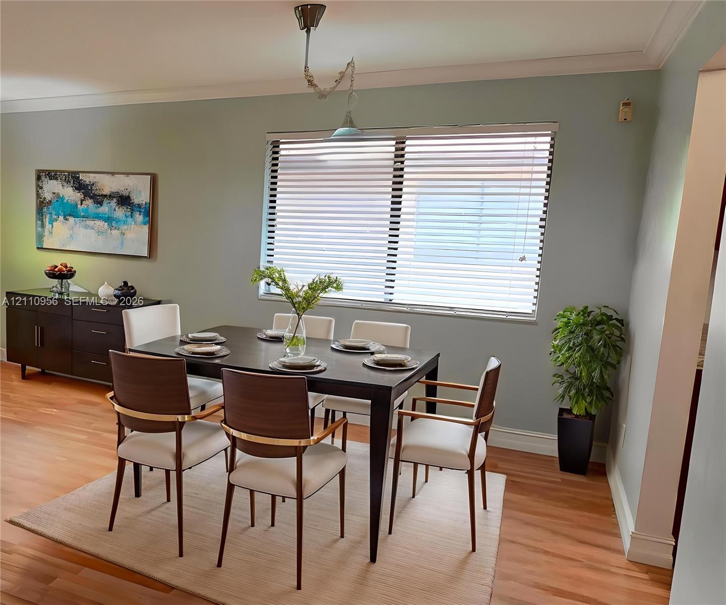 Dining area featuring wood-finish flooring, crown molding, a large window with horizontal blinds, and a suspended pendant light fixture