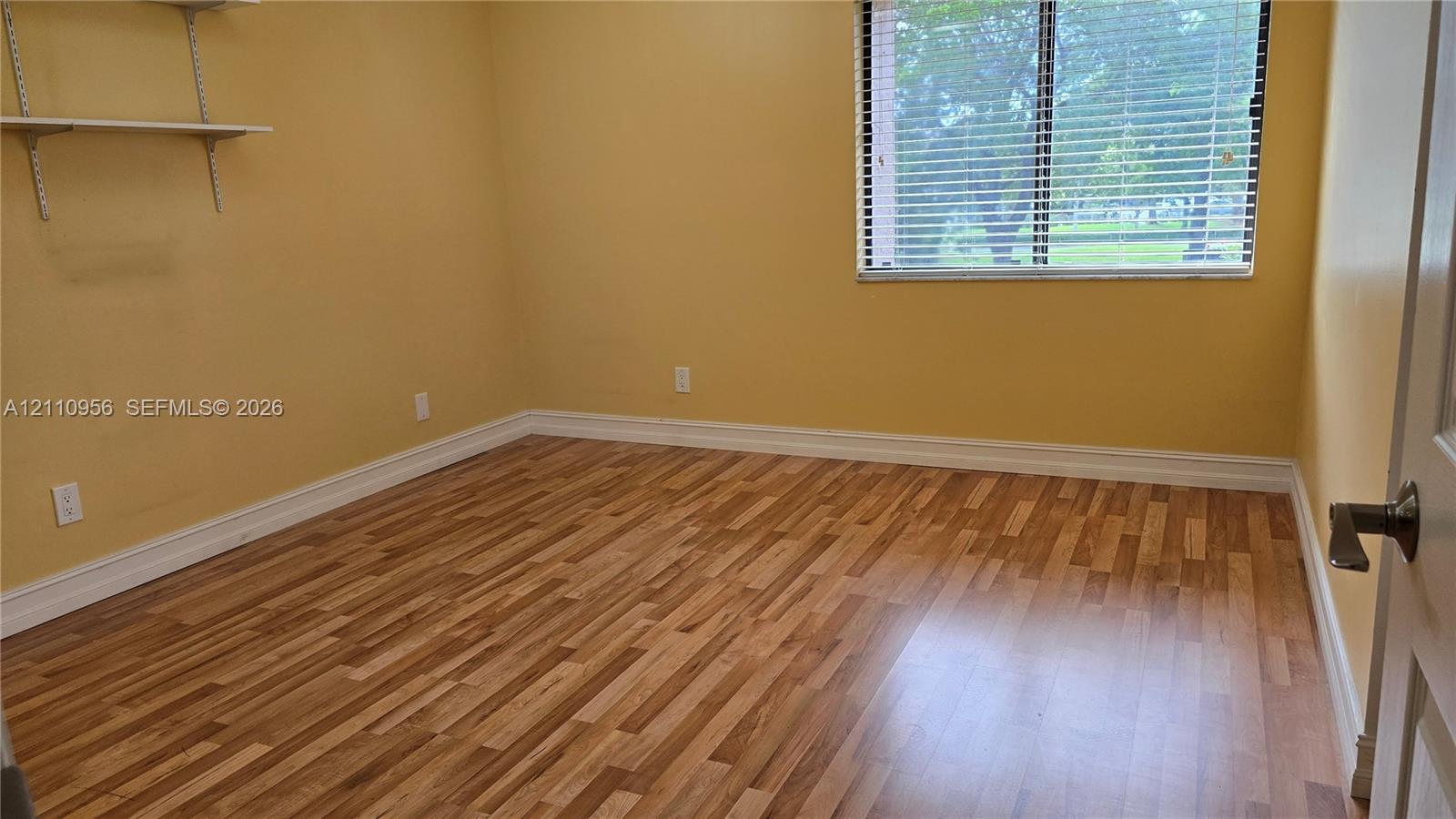 Wood-finish flooring, wall-mounted shelving, and horizontal window blinds