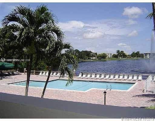 Swimming pool featuring a paved deck, perimeter fencing, and mature palm trees, positioned alongside a lake with a fountain