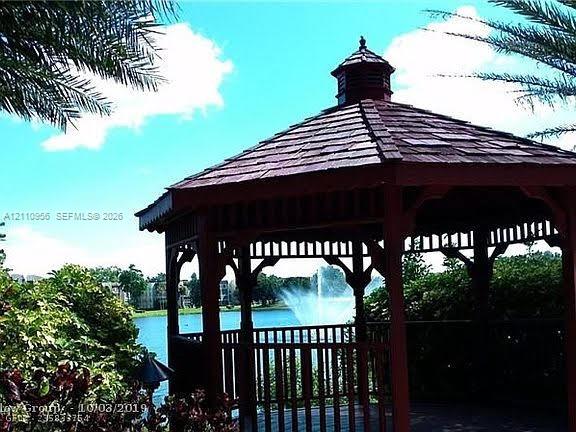 Octagonal wood-framed gazebo featuring a tiered roof with wood-shingle detailing, perimeter railing, and a waterfront location with a fountain