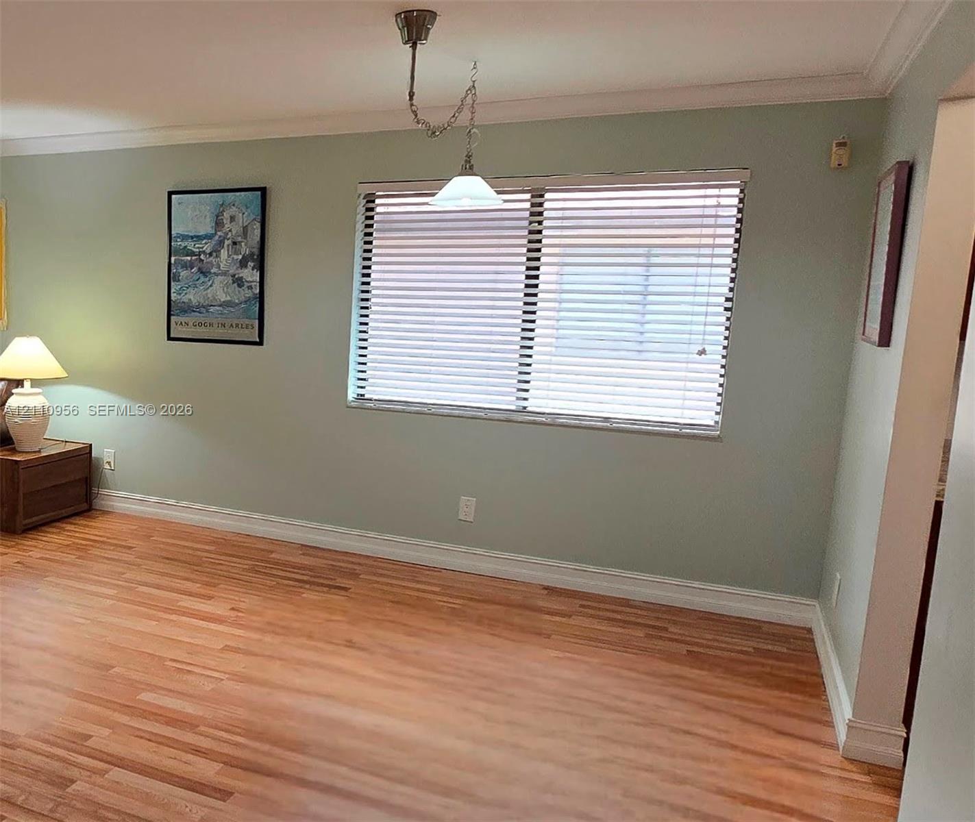 Living area featuring wood-finish flooring, crown molding, and a central pendant light fixture