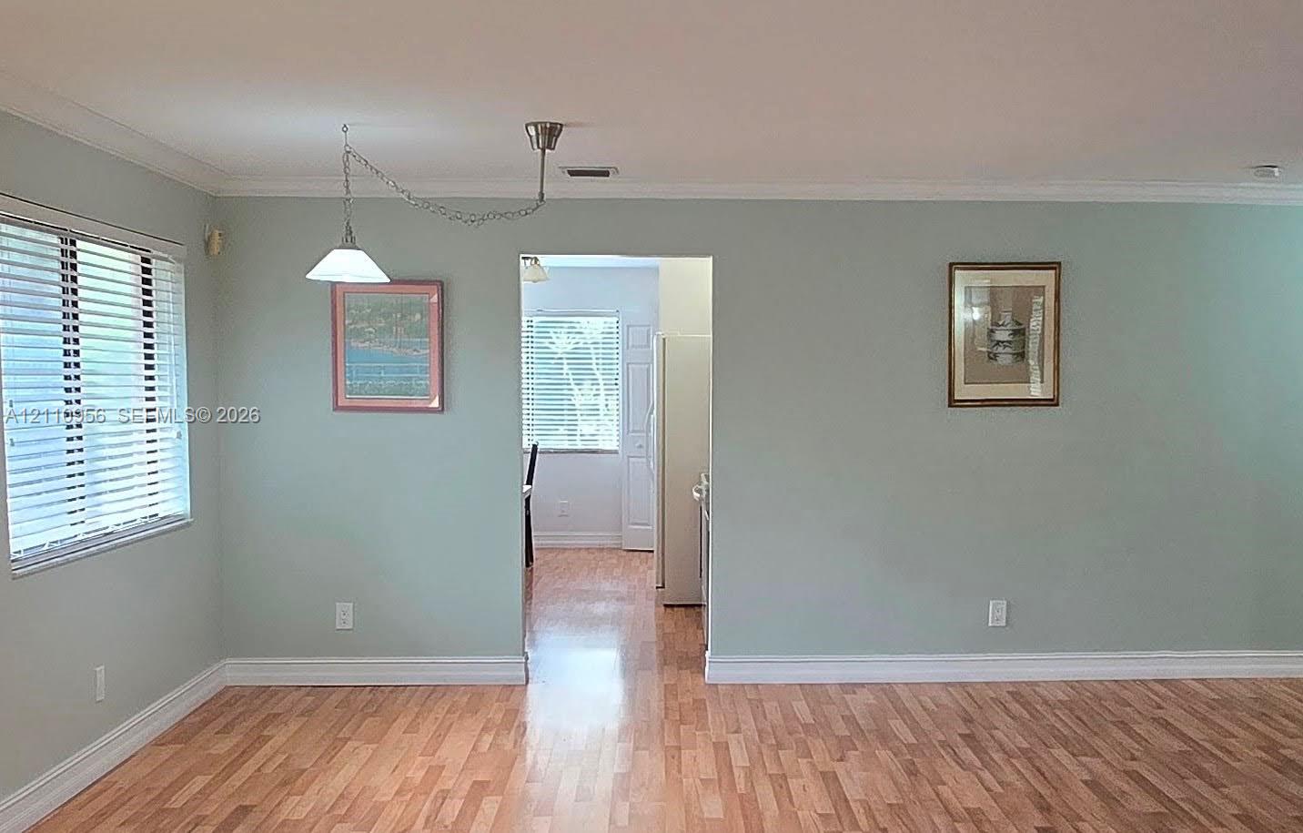 Interior space featuring wood-finish flooring, crown molding, and a suspended cone pendant light fixture