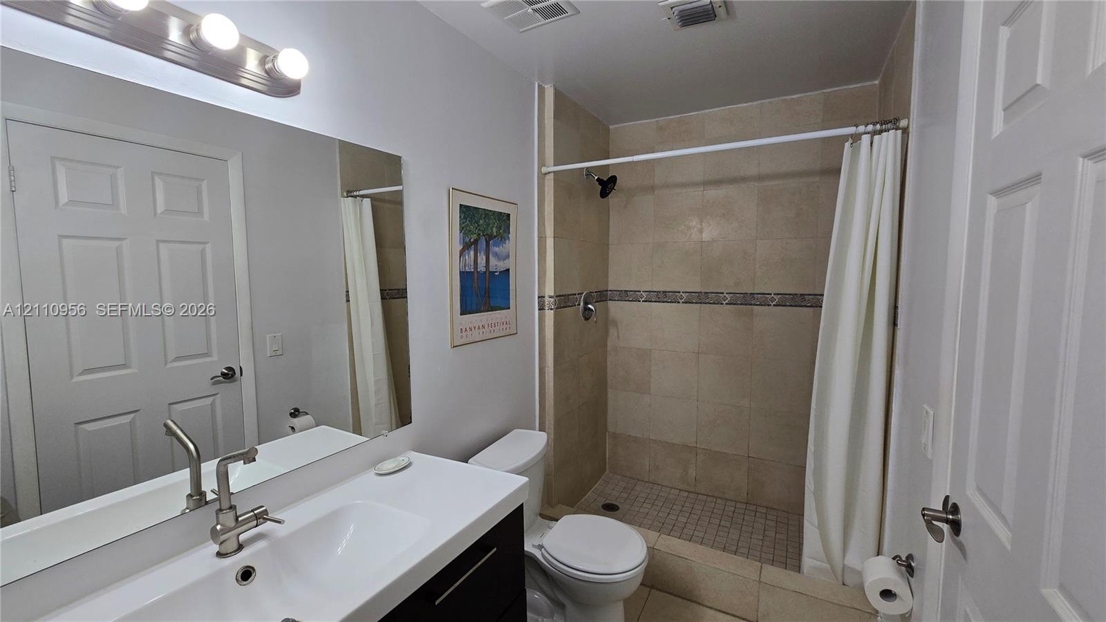 Bathroom featuring a dark wood-finish vanity, white integrated sink, rectangular wall mirror, and walk-in shower with stone-finish wall tiles