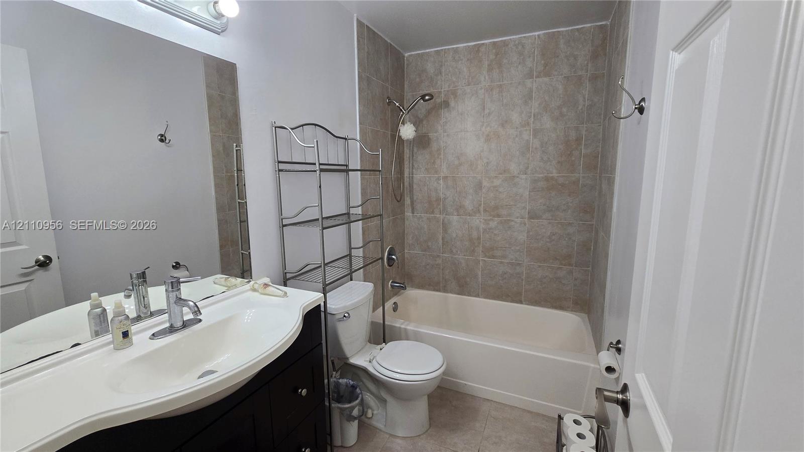 Bathroom featuring a vanity with an integrated basin, a polished metal faucet, a large wall-mounted mirror, a tub-shower combination with tile surround, and a neutral-toned toilet