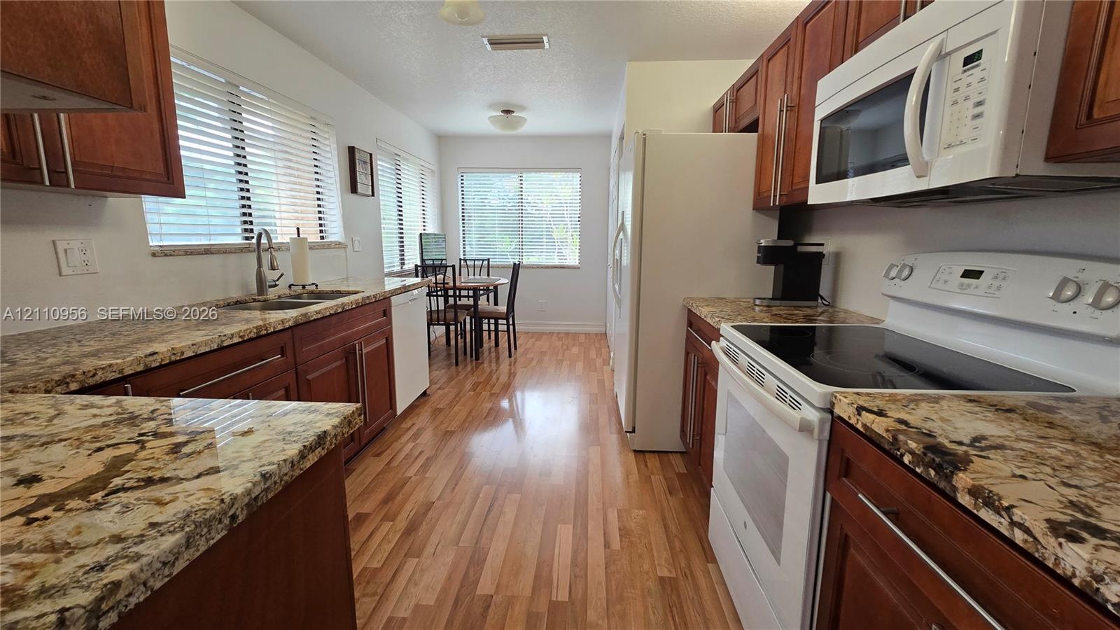 Kitchen featuring wood cabinetry, stone countertops, wood-finish flooring, and white built-in appliances