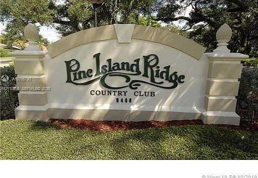 Stucco monument sign featuring decorative finials, tiered masonry pillars, and mature landscaping