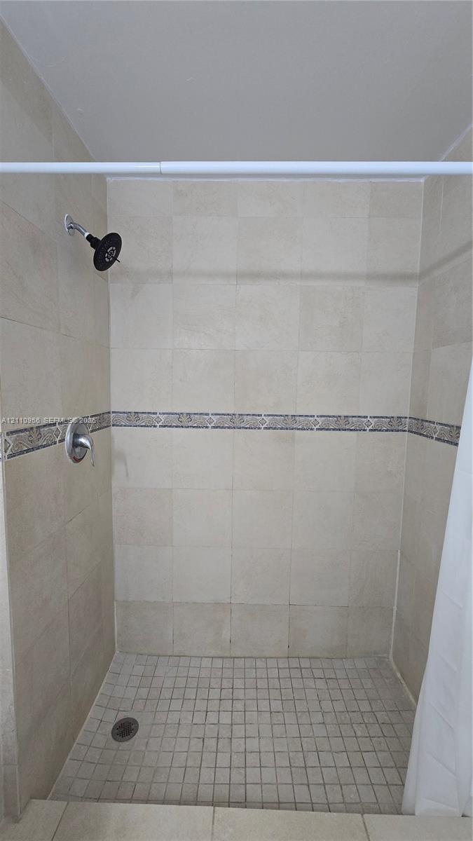 Walk-in shower featuring floor-to-ceiling tile, decorative accent trim, a mosaic tile floor, and a wall-mounted showerhead