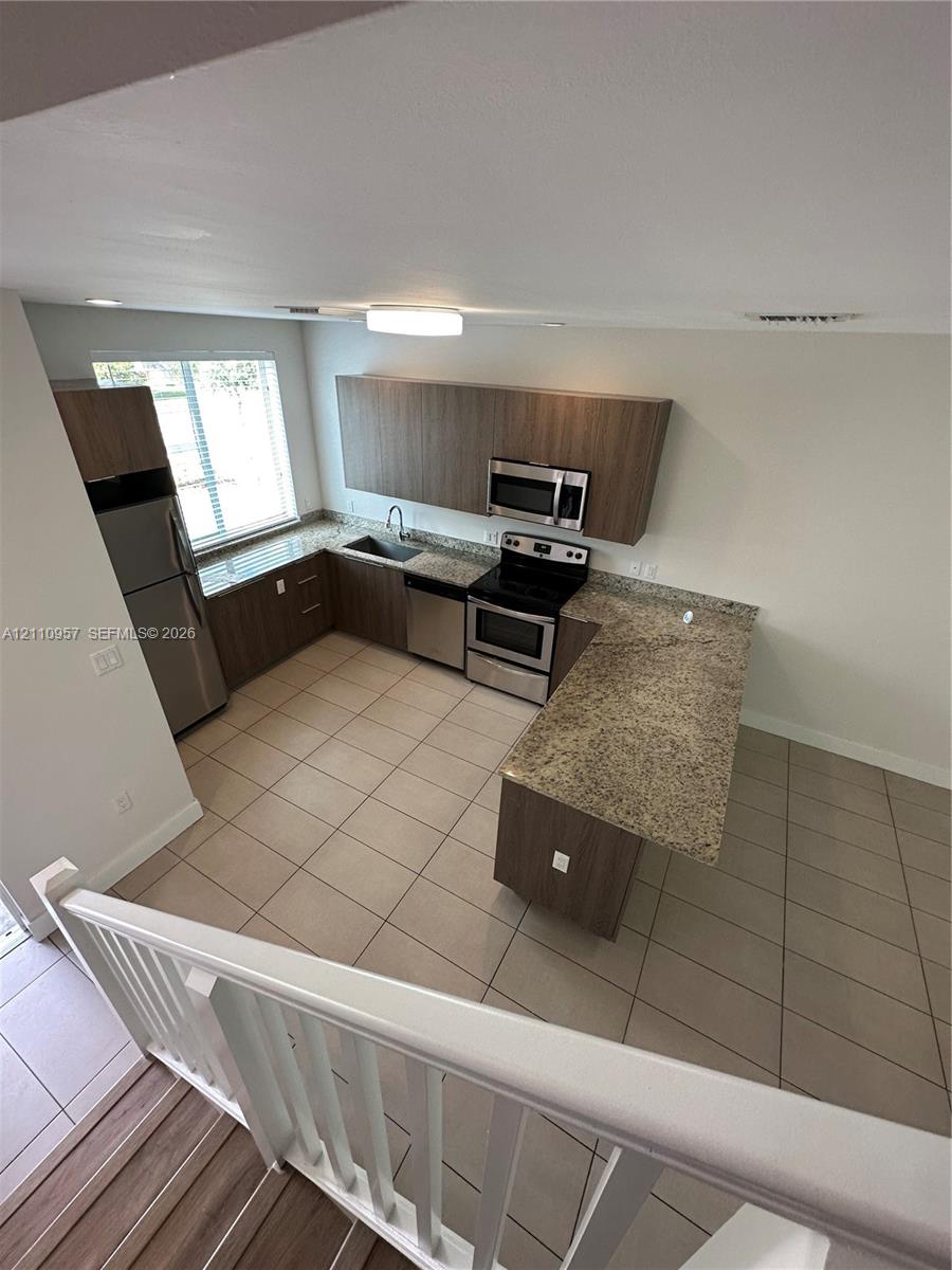 Kitchen featuring flat-panel wood-finish cabinetry, stone-surface countertops, stainless steel appliances, ceramic tile flooring, and a peninsula with counter seating