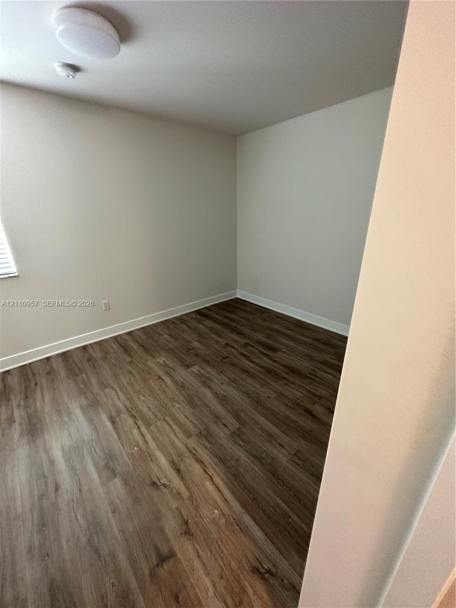 Room with wood-finish flooring, neutral-toned walls, and a ceiling-mounted light fixture