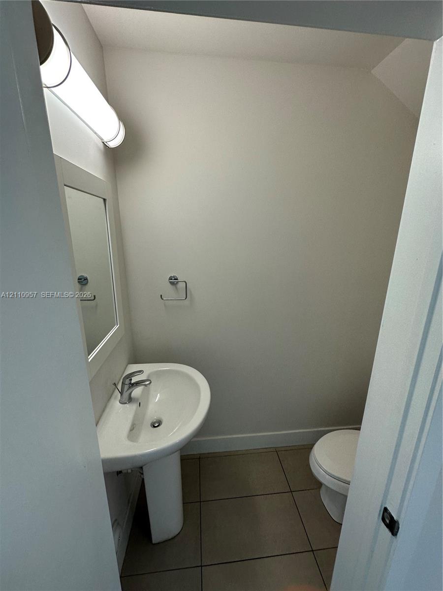 Powder room featuring a pedestal sink, wall-mounted light fixture, framed mirror, and tile flooring