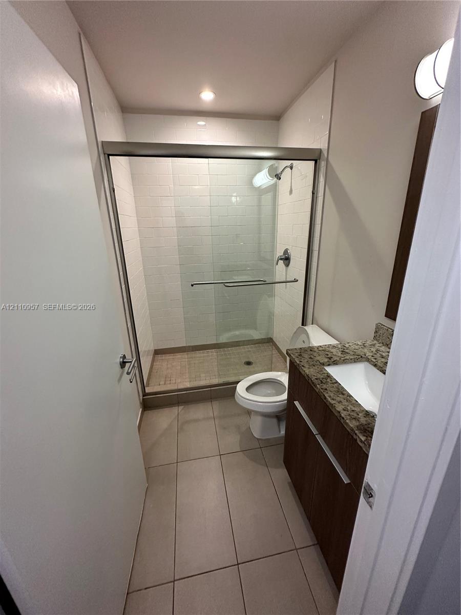 Bathroom featuring a glass-enclosed shower with subway tile surround, vanity with stone-finish countertop, undermount sink, and large-format tile flooring