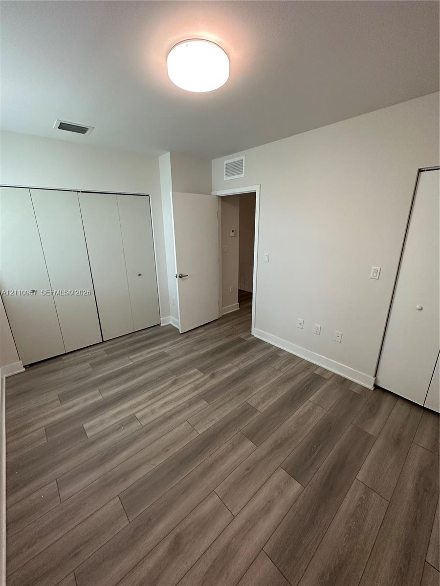 Room featuring wood-finish flooring, dual bi-fold door closets, neutral wall paint, and a flush-mount overhead light fixture