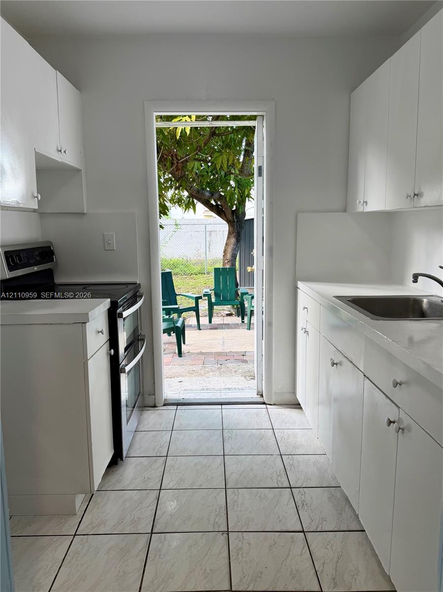 Kitchen featuring white cabinetry, solid-surface countertops, tile flooring, and integrated black range Kitchen featuring white cabinetry, solid-surface countertops, tile flooring, and integrated black range