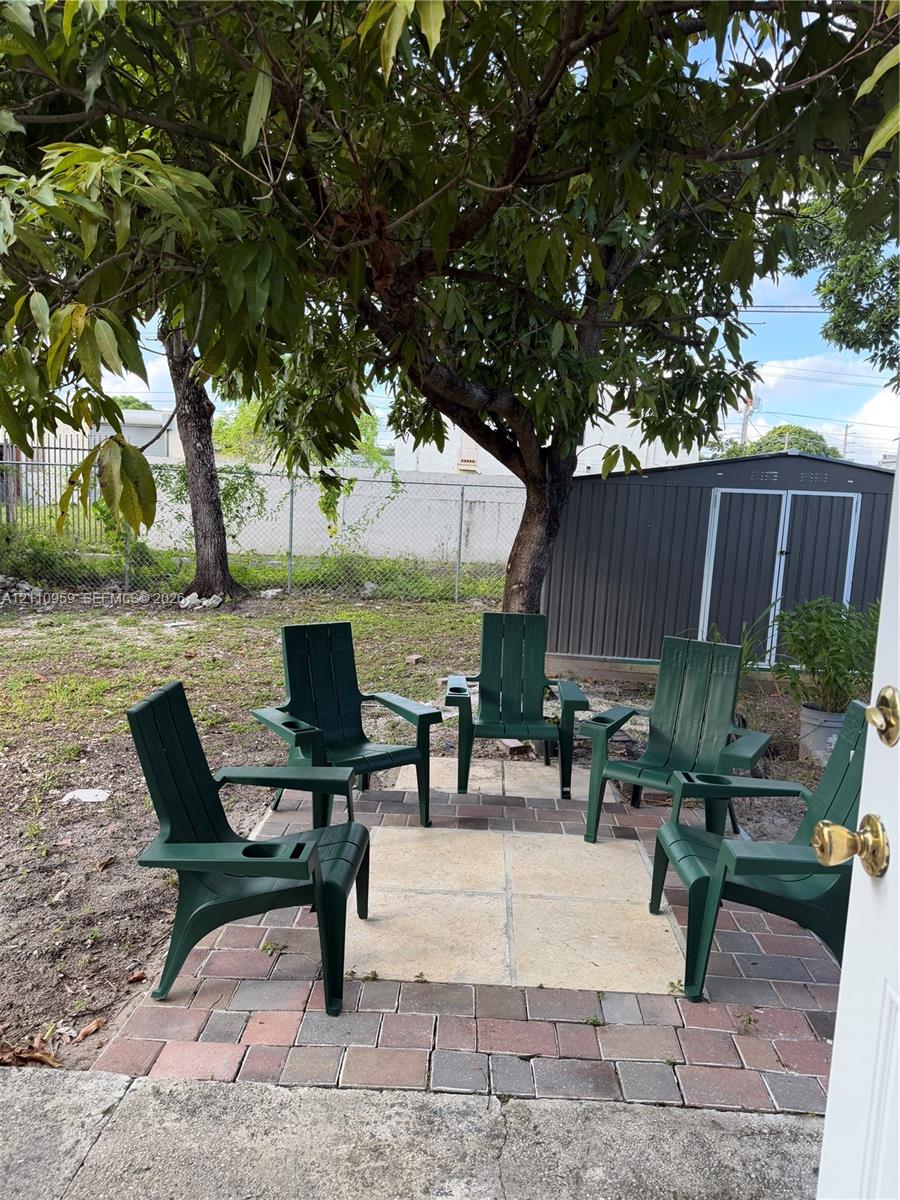 Rear yard featuring a paver patio with a central inlay, a metal storage shed, mature trees, and chain-link perimeter fencing