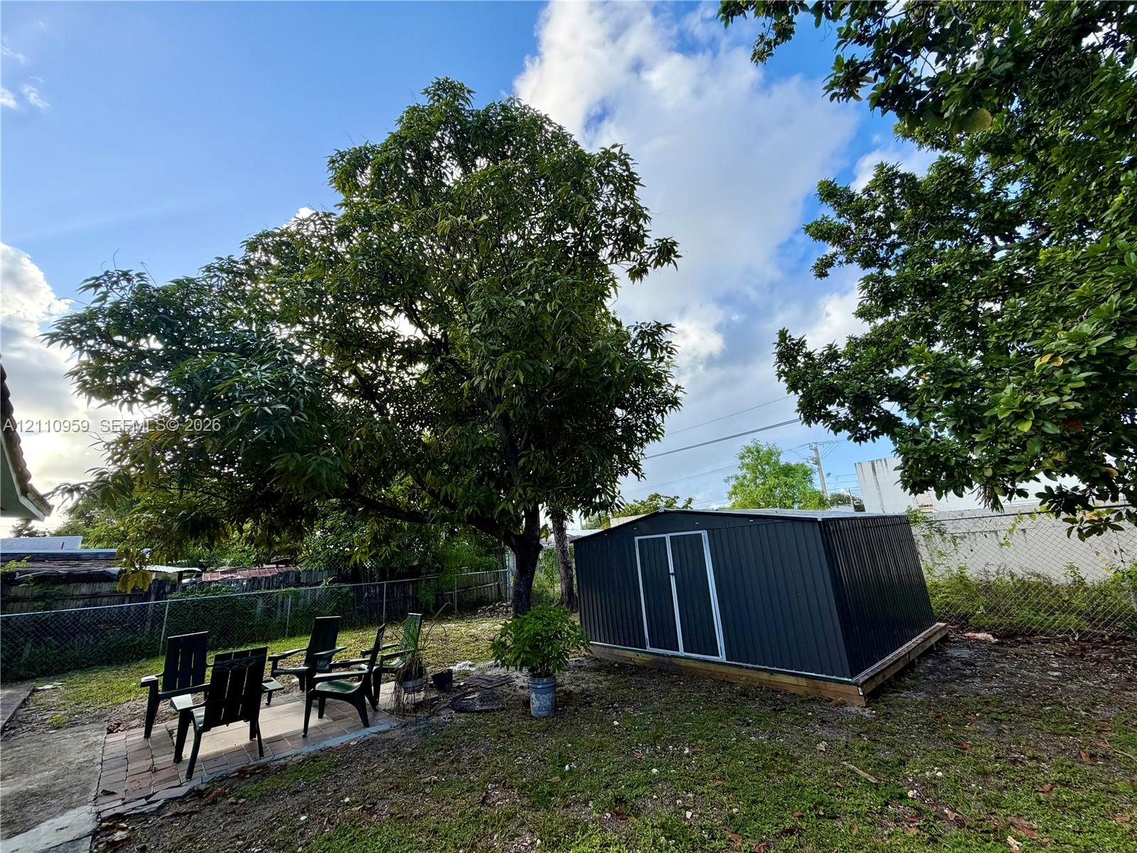 Backyard space featuring a metal storage shed, brick paver patio, mature tree, and chain-link fencing