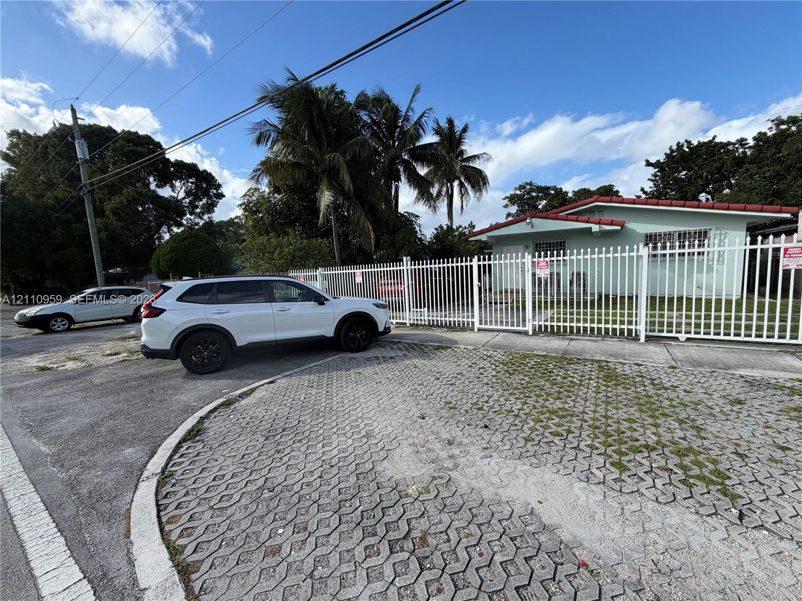 Exterior featuring a gated perimeter fence, concrete paver driveway, and mature palm trees