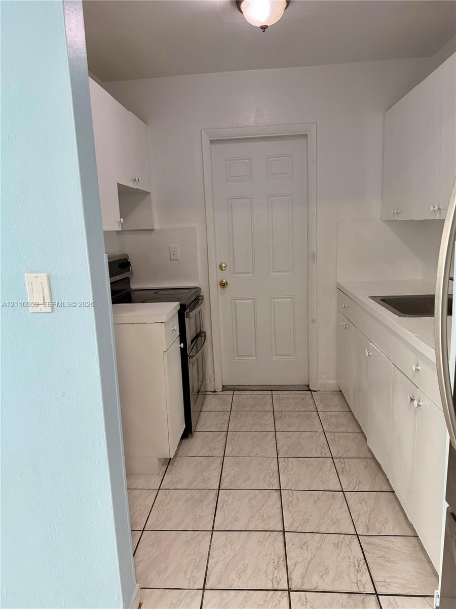 Kitchen featuring white cabinetry, solid-surface countertops, tile flooring, stainless steel range, and a flush-mount ceiling light fixture Kitchen featuring white cabinetry, solid-surface countertops, tile flooring, stainless steel range, and a flush-mount ceiling light fixture