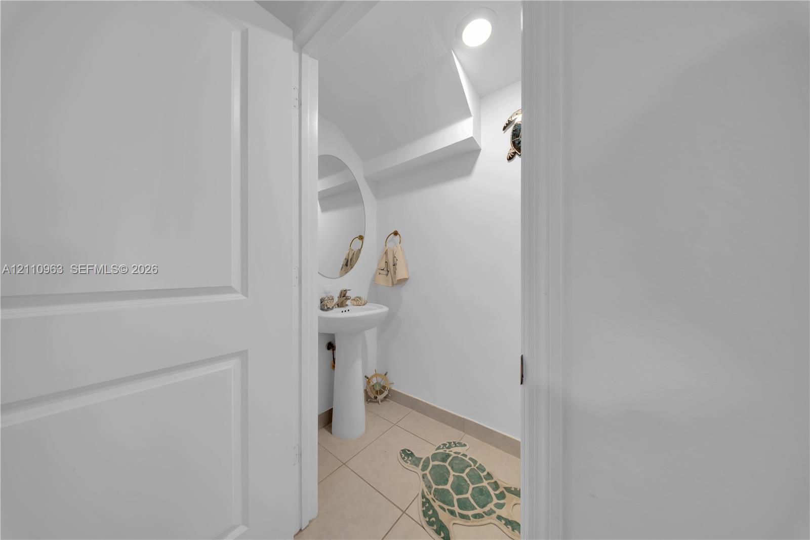 White pedestal sink with a metallic faucet, oval wall mirror, recessed ceiling lighting, and tile flooring