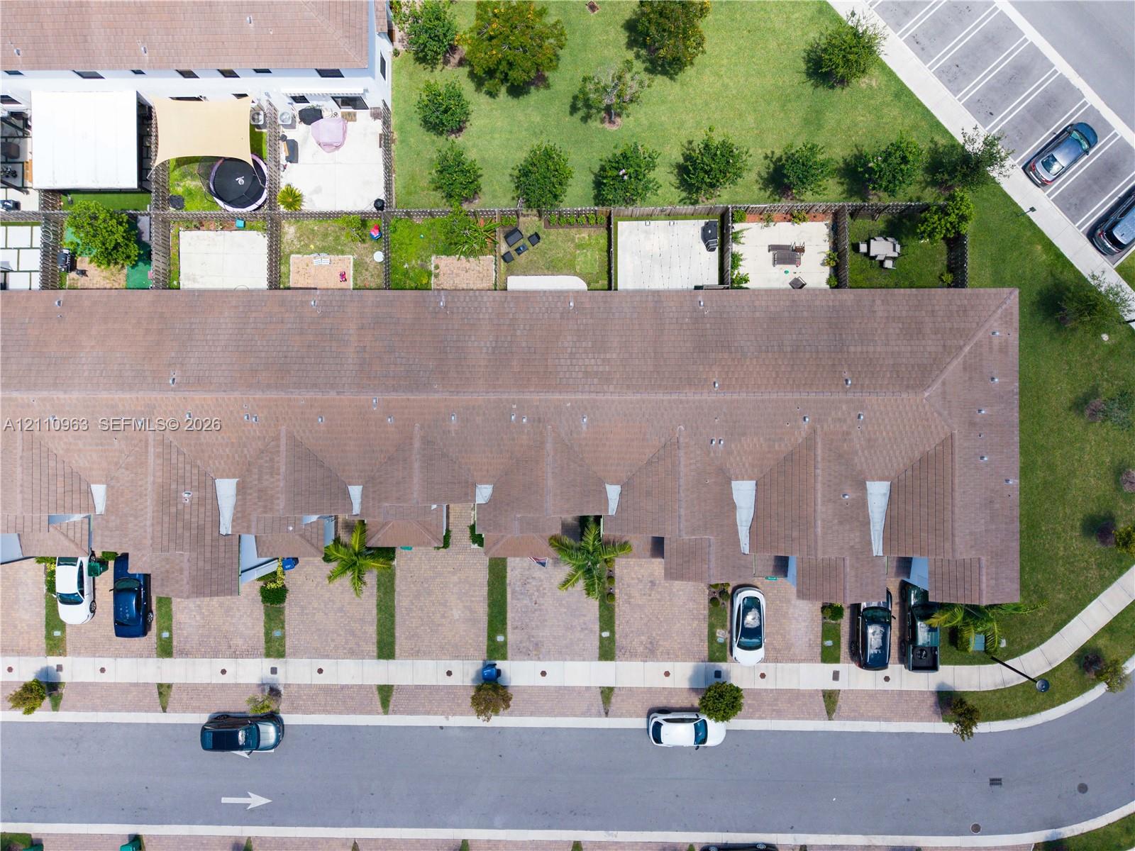 Aerial perspective of a multi-unit property featuring a shingled hip roof, paved driveways, and private fenced rear patios