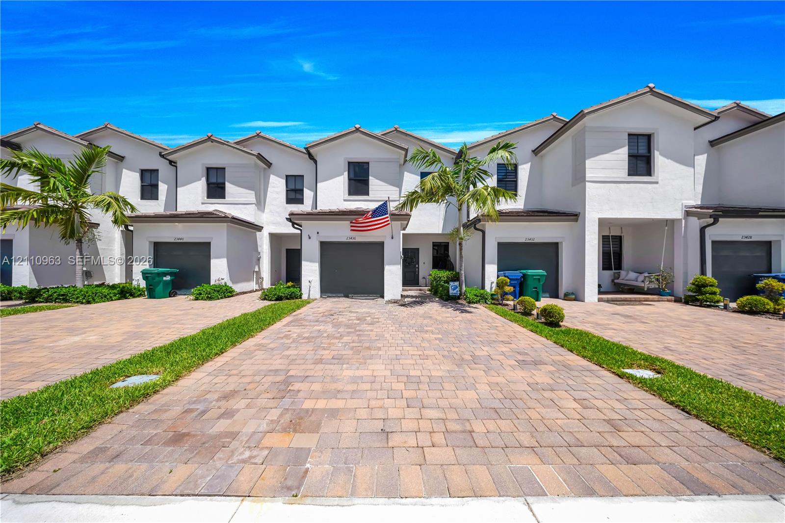 Stucco exterior featuring multi-unit architectural design, paved stone driveways, attached garage bays, and landscaping