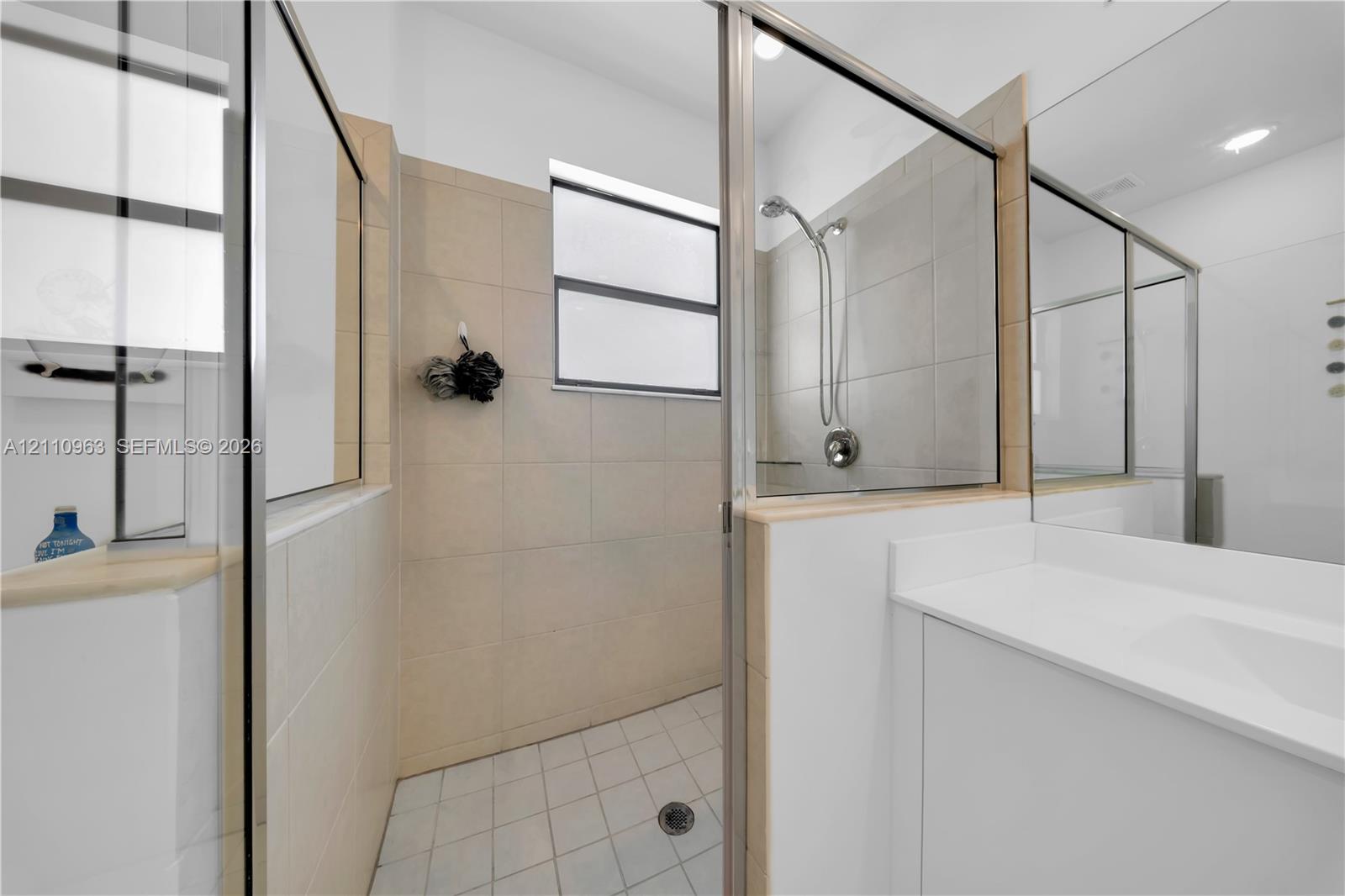 Walk-in shower featuring glass paneling, tile wall surround, and metal shower hardware, paired with a white vanity featuring a solid surface countertop