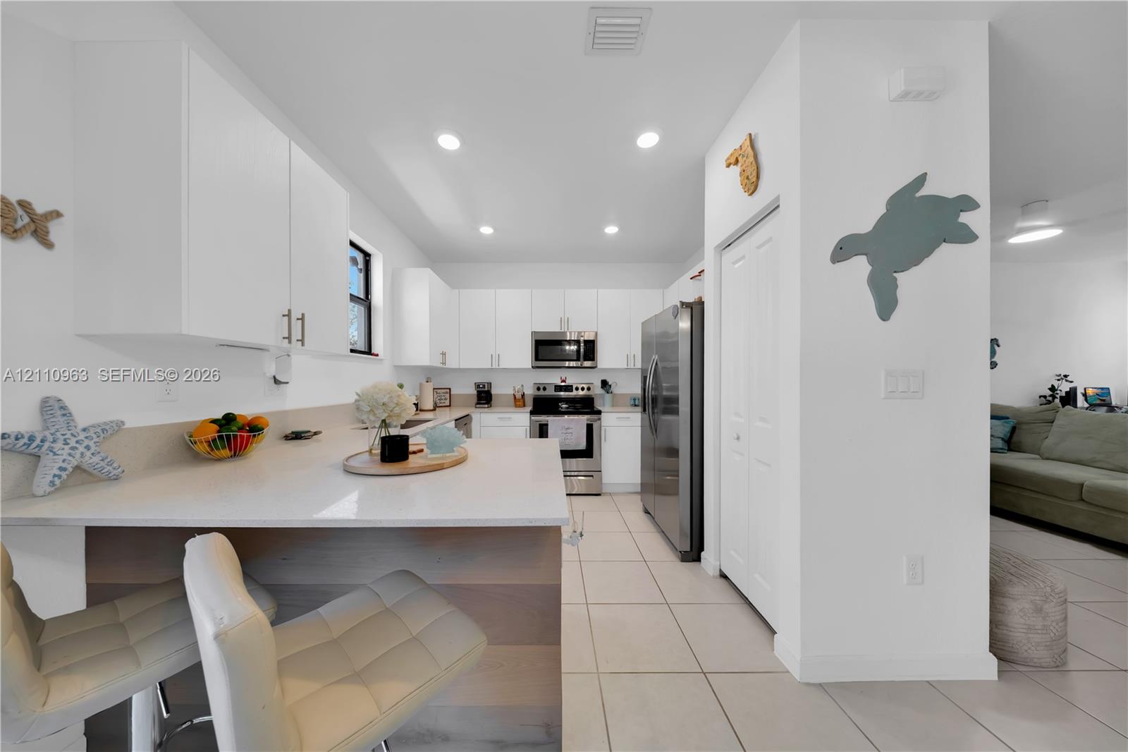 Kitchen featuring white cabinetry, quartz countertops, a stone-finish waterfall edge island, recessed lighting, and stainless steel appliances