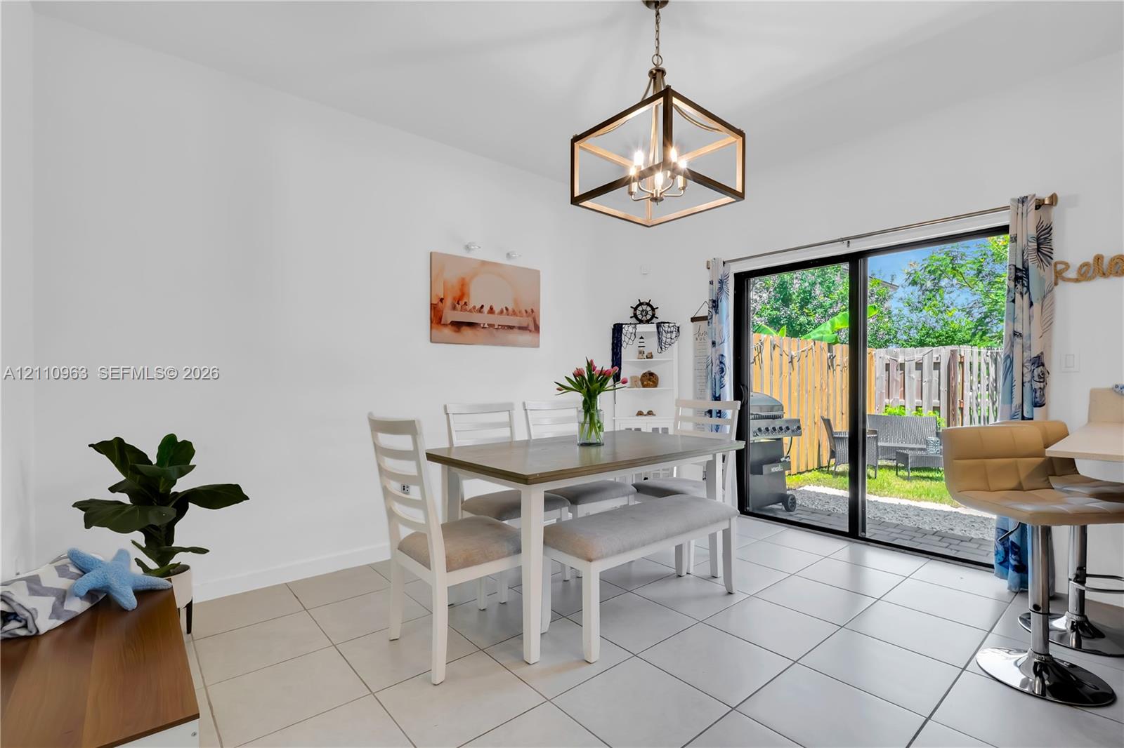 Dining area featuring neutral tile flooring, a geometric metal chandelier, and a sliding glass door providing external access to a fenced patio