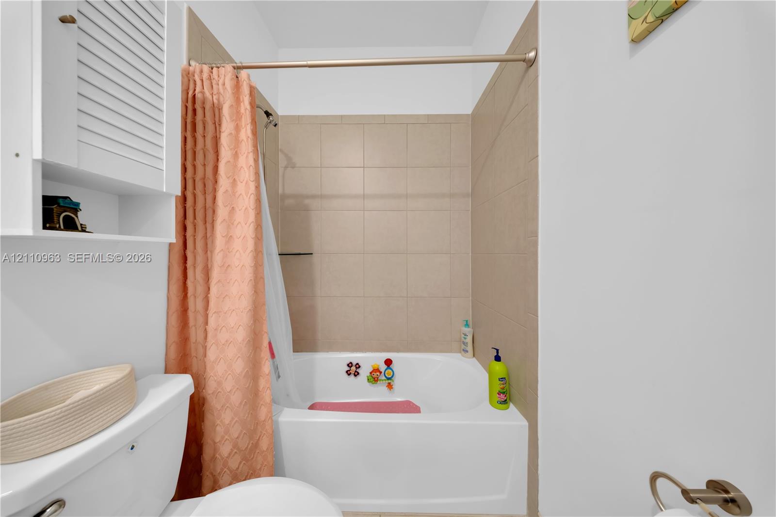 Bathroom featuring a tub with a tile surround, a built-in shutter-style wall cabinet, and metallic hardware