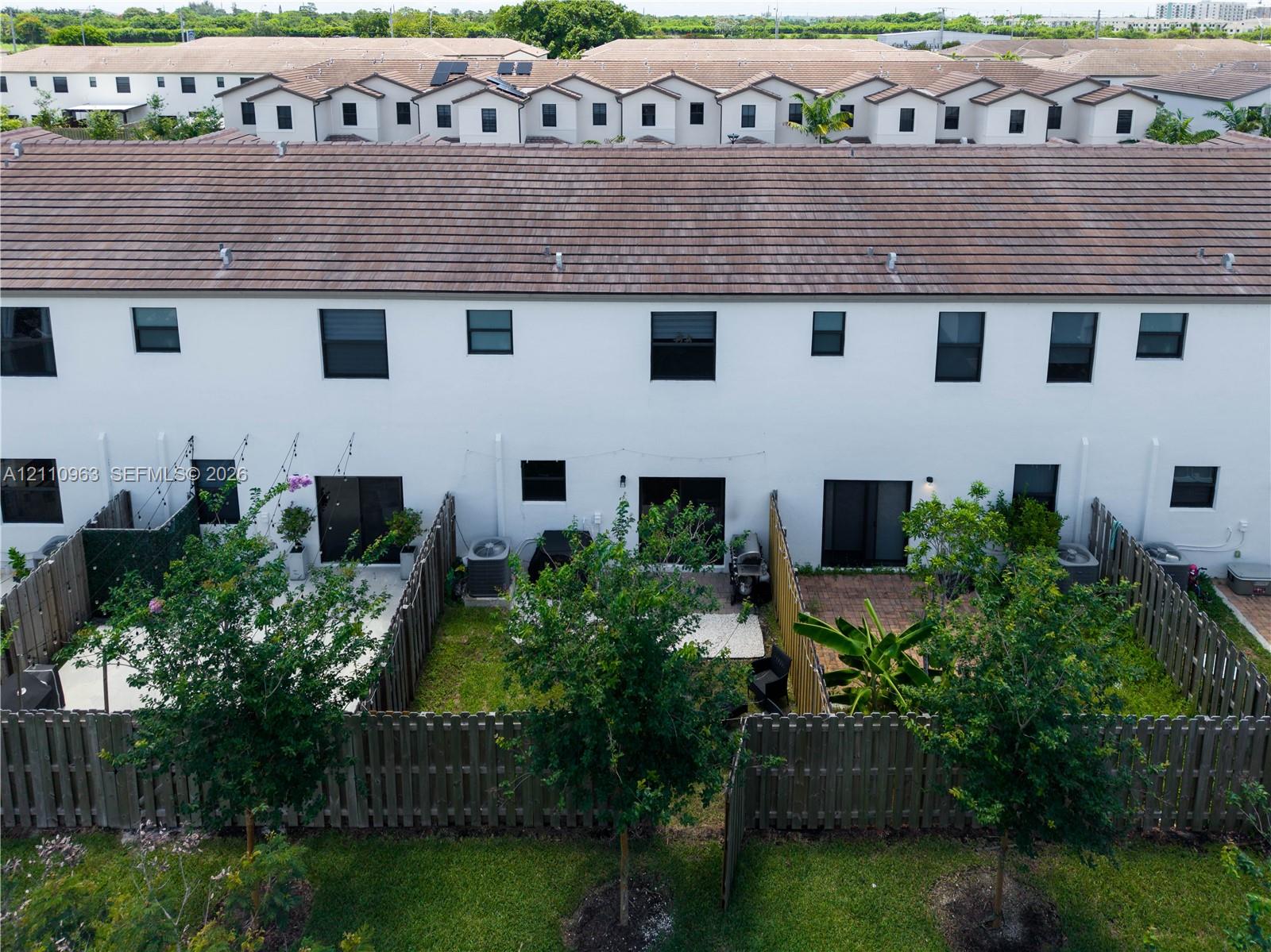 Two-story townhome exterior featuring white stucco siding, a tiled roof, private fenced rear patios, and rear-entry sliding glass doors