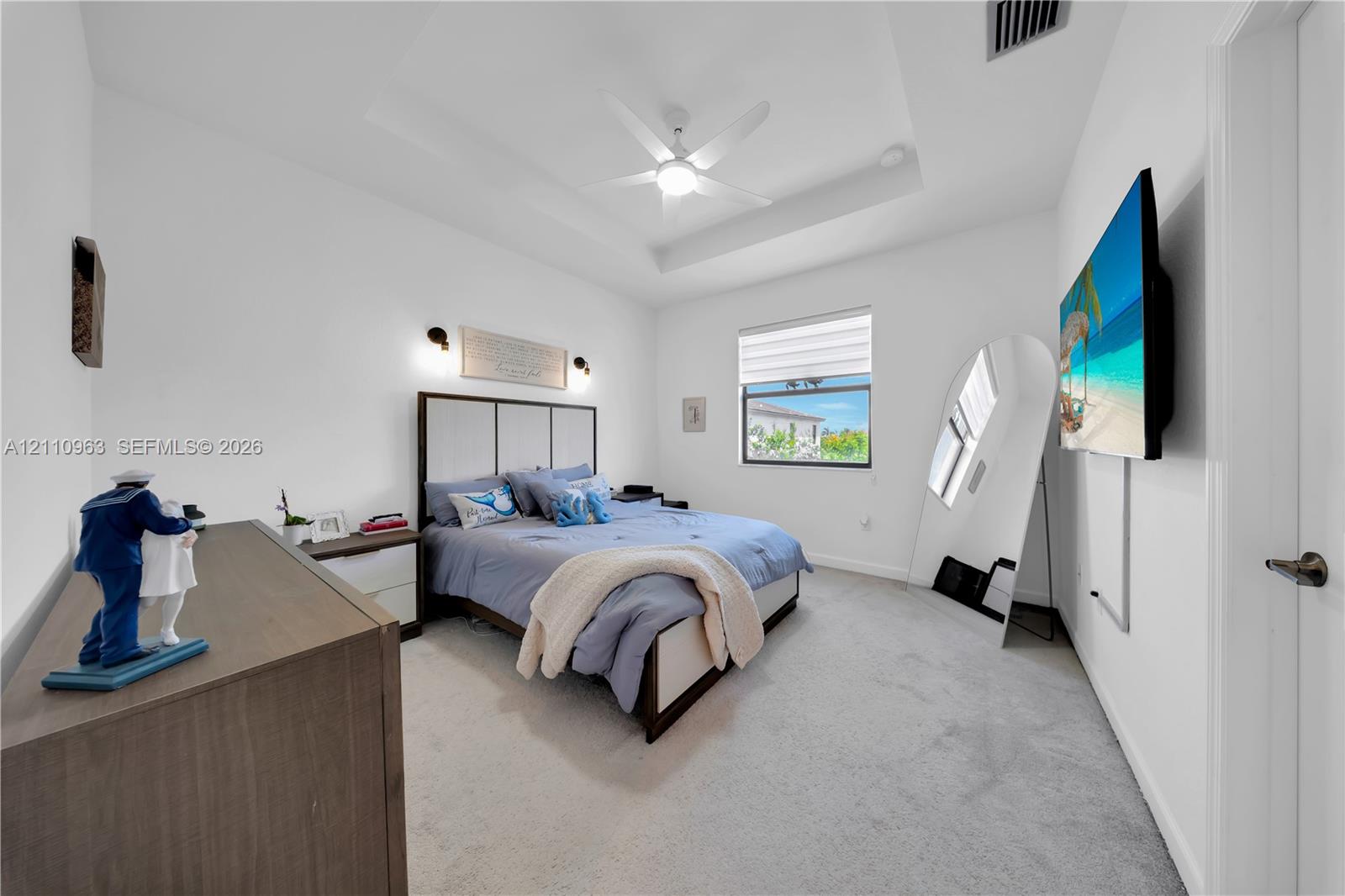 Tray ceiling with central paddle fan, wall-mounted light fixtures, and neutral carpeting