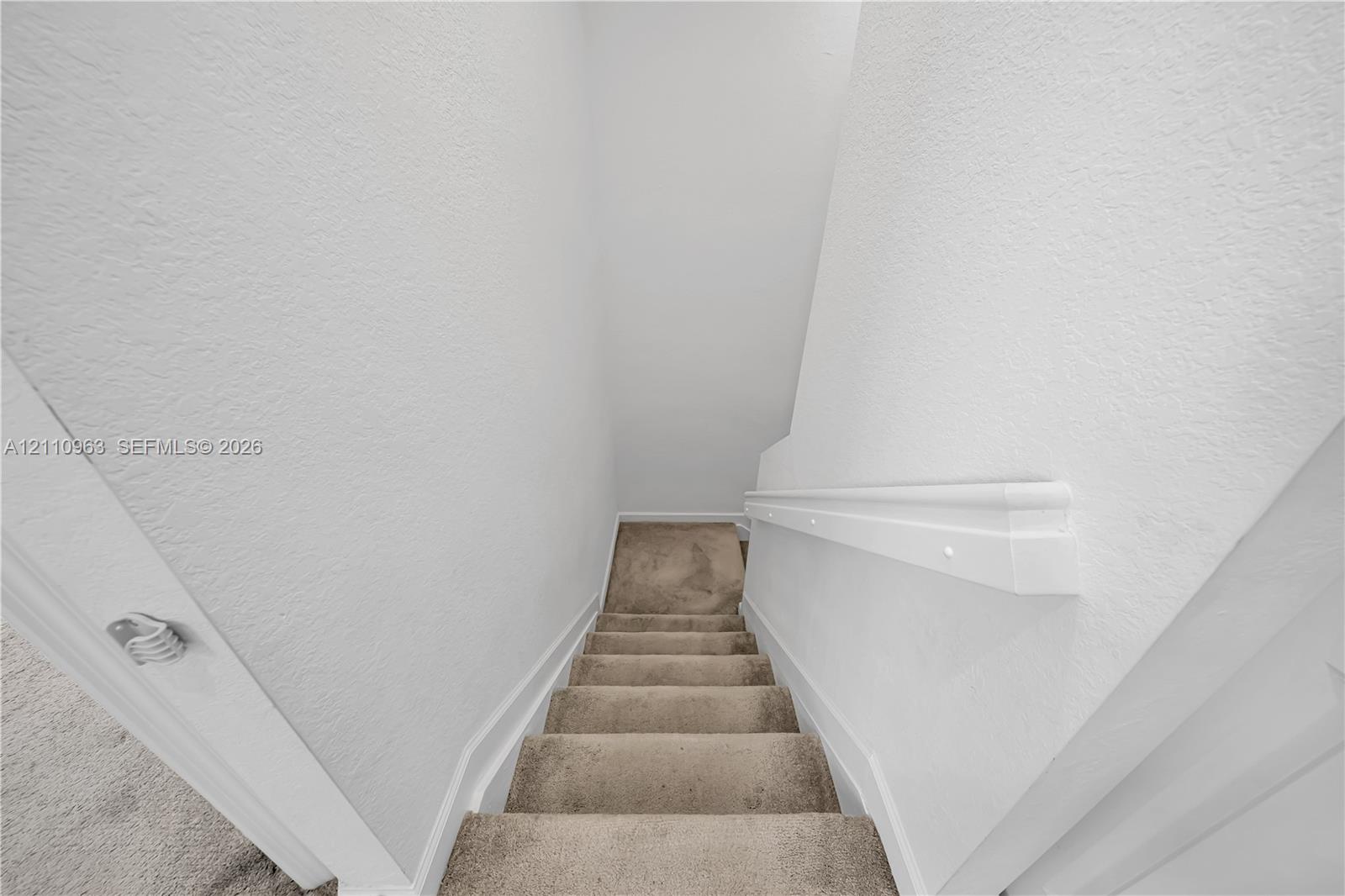 Staircase featuring neutral-toned carpeting and a painted wall-mounted handrail