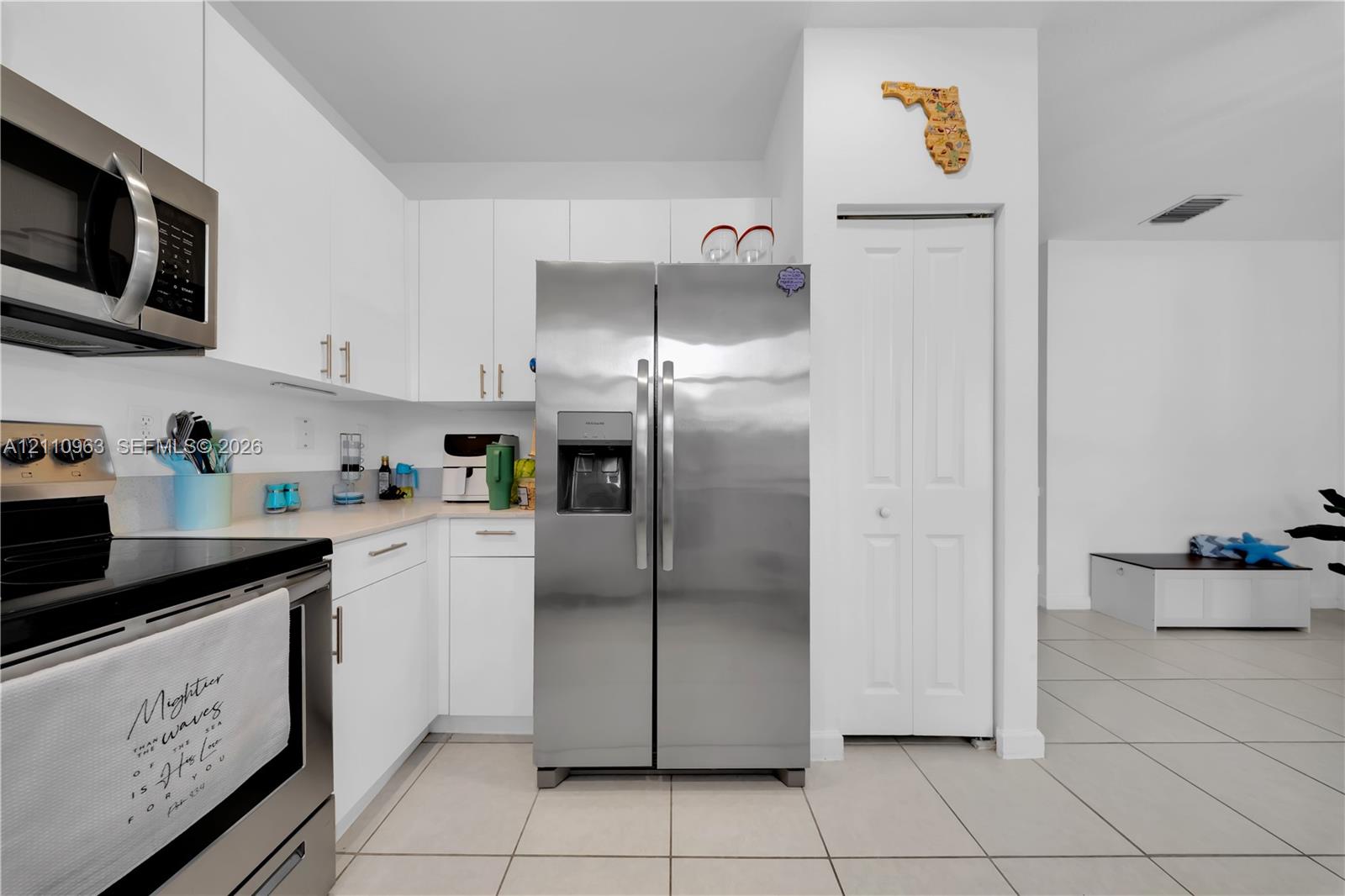 Kitchen featuring white flat-panel cabinetry, stainless steel appliances, neutral tile flooring, and a pantry with a bi-fold door