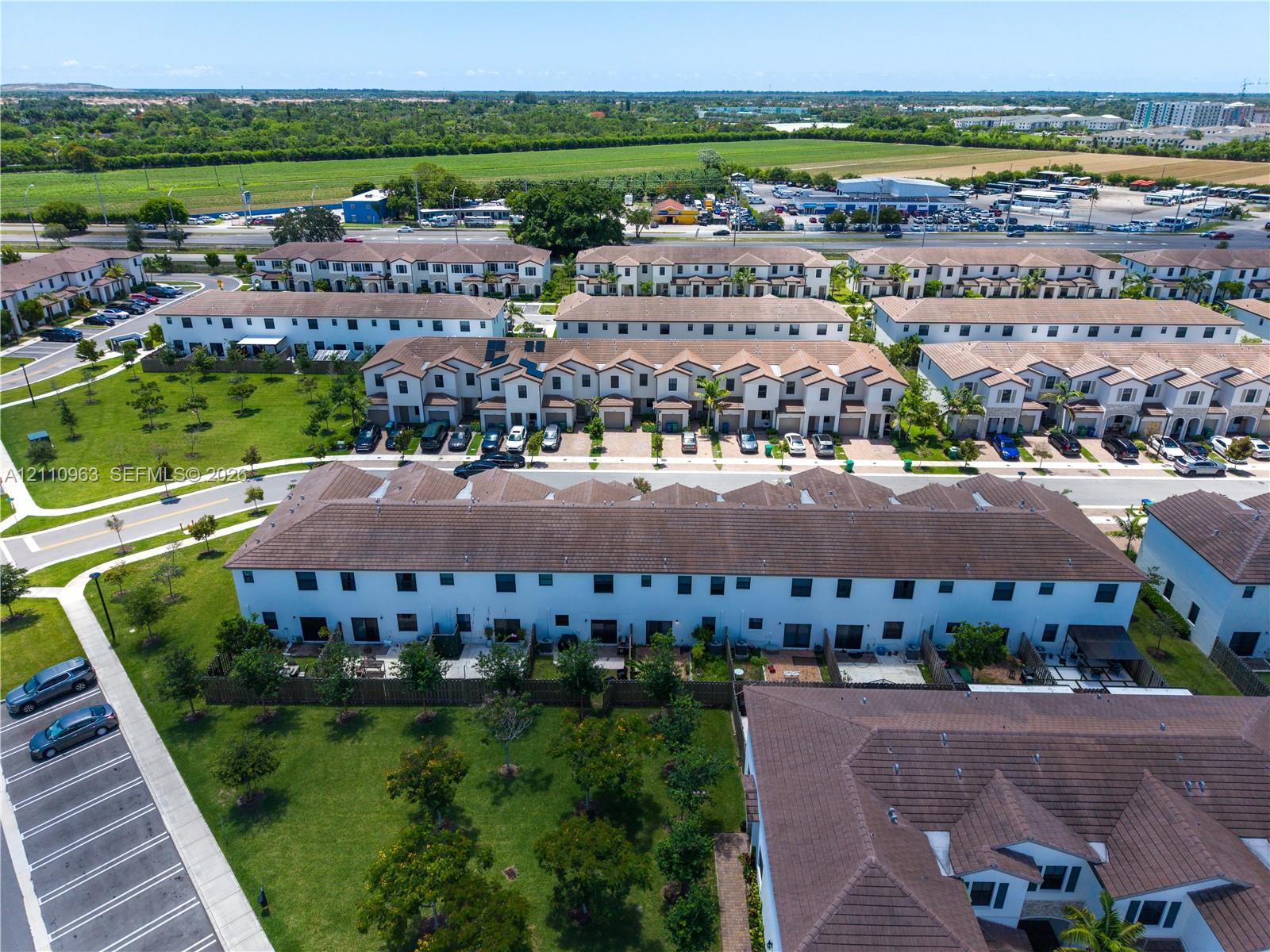 Aerial perspective of a multi-unit residential community featuring tiered tile roofing, paved parking areas, and expansive surrounding green spaces