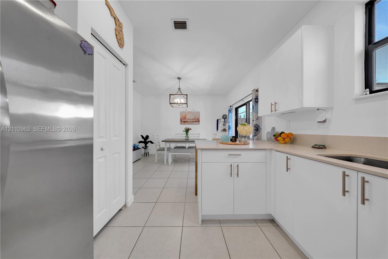 Kitchen featuring white cabinetry, stainless steel appliances, solid surface countertops, tile flooring, and a pendant light fixture