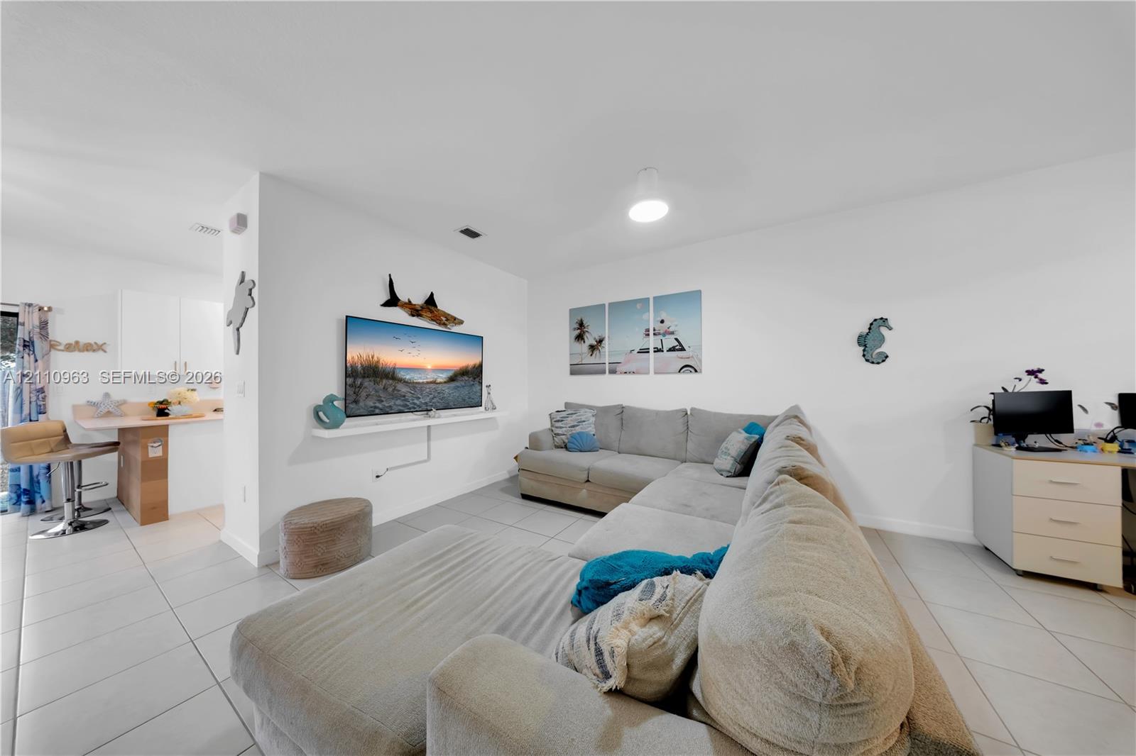 Open-concept space featuring light-toned tile flooring, recessed ceiling lighting, a wall-mounted display shelf, and a built-in kitchen peninsula with a countertop